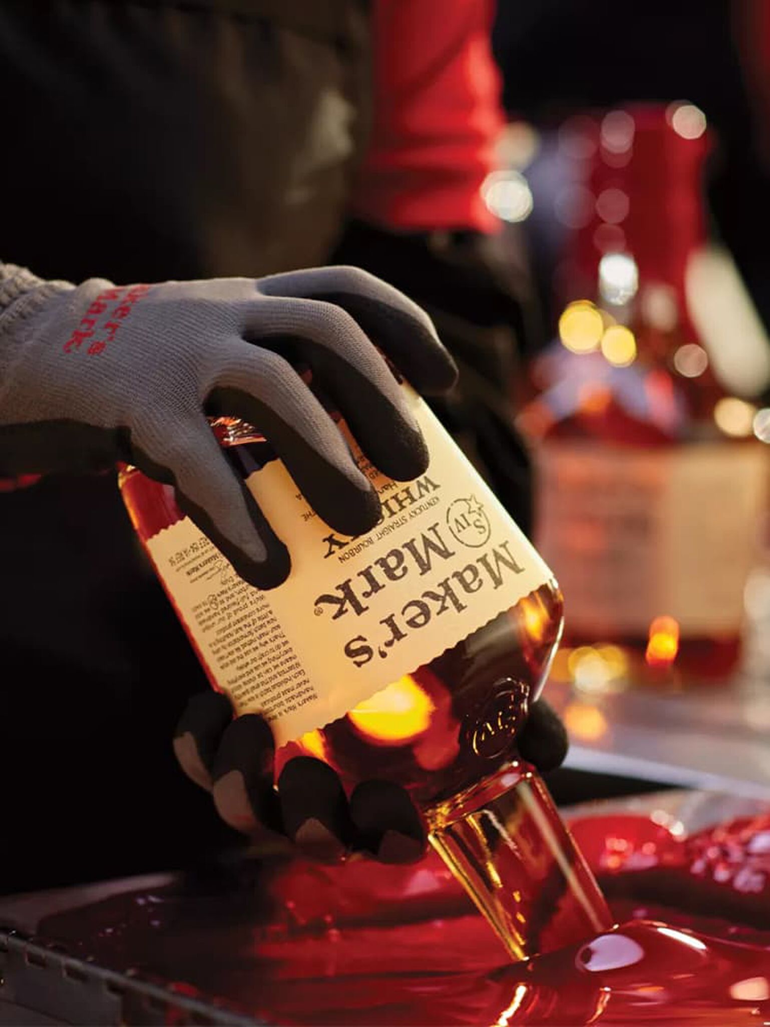 A bottle of Maker's Mark is dipped into a vat of the iconic red wax that seals the bottle